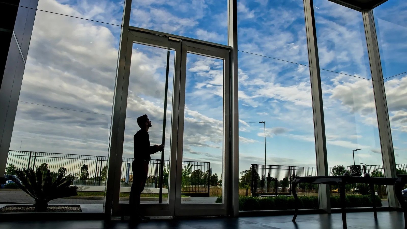 Acceso vidriado. Puerta y paños fijos de gran altura que se leen como un único plano transparente.